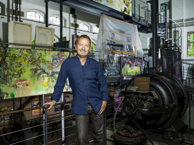 It shows the artist in his studio with his collection of artworks.