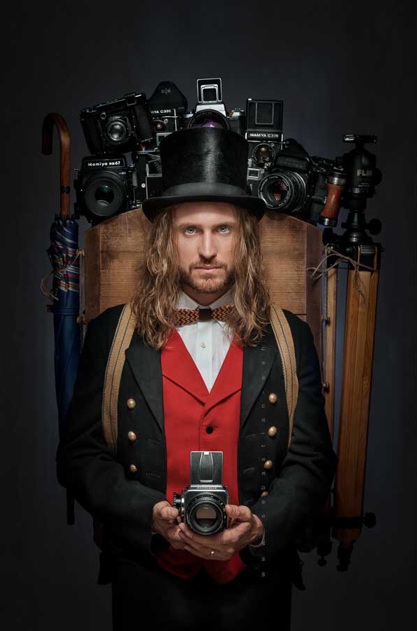 It shows the artist with his photographic cameras, in an elegant black suit, red jacket, white shirt and top hat.